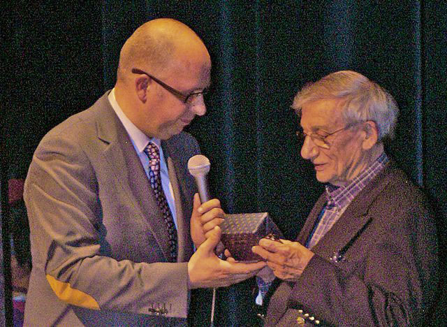 A harmonica player receiving a gift on stage at a festival in the Netherlands