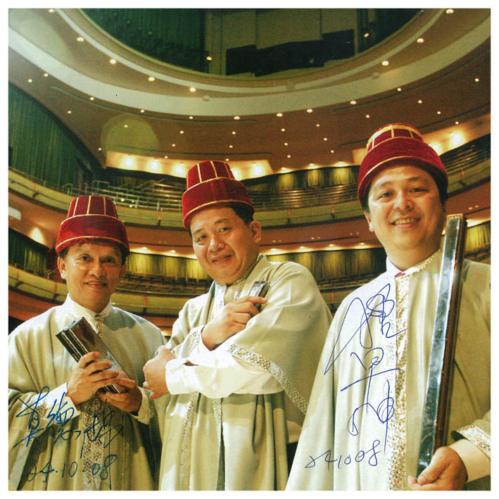 Three harmonica players in traditional costume in a concert hall, signed photo