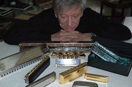 A harmonica player leaning behind a collection of harmonicas of all sizes