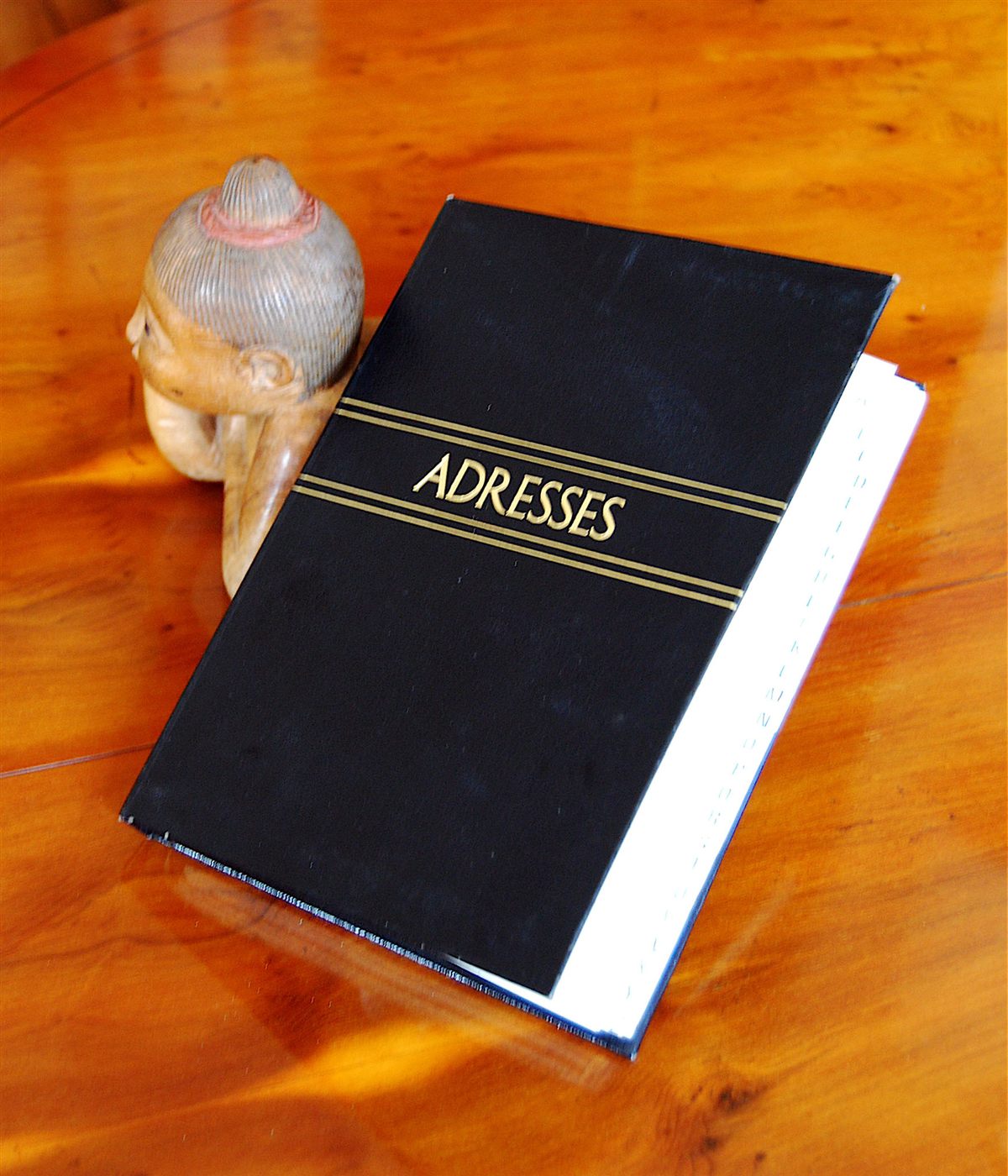 Carnet d'adresses noir posé sur une table en bois, près d'une statuette